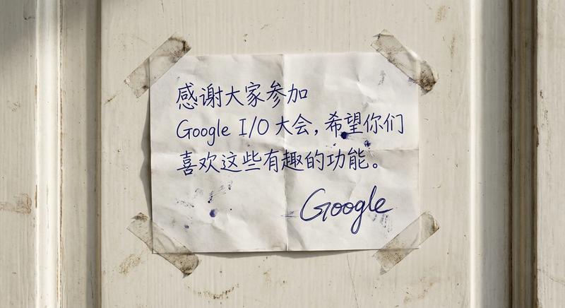 创作一张逼真的手写感谢便条，其外形犹如一张微皱的收据，贴在一扇门外。便条四角各用一小片透明胶带固定，胶带边缘微微翘起。便条上手写着一条感谢语：“感谢大家参加 Google I/O 大会，希望你们喜欢这些有趣的功能。”笔迹应略带瑕疵，线条粗细和力度不均，以模仿圆珠笔在薄纸上书写的效果。落款是一个手写体的风格化“Google”徽标，字迹与正文保持一致。门是中性色调（如浅灰、米白或浅木纹）的，略显陈旧，表面有轻微的划痕或污渍等使用痕迹。光线为自然光，投下柔和的阴影，凸显出门和便条的质感。整个场景旨在营造一种温暖、真诚和感谢的氛围，仿佛是某人亲手留下的一则私人留言。