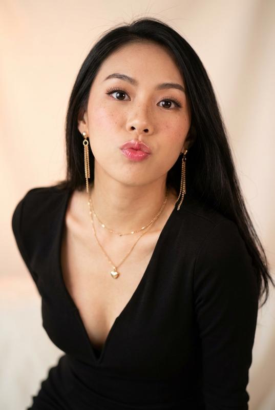{
  "style": "ultra-realistic celebrity portrait, soft romantic photography",
  "subject": {
    "identity": "based on uploaded reference",
    "gender": "female",
    "age": "young adult",
    "pose": "tilting head slightly to the side, looking up at camera through lashes, playful and cute posture",
    "expression": "pouting lips, acting cute, puppy eyes, innocent look, 'sajiao' vibe",
    "facial_details": {
      "eyes": "big imploring eyes, looking up, soft gaze",
      "mouth": "pouted lips, slight pout",
      "cheeks": "faint blush",
      "freckles": "visible natural freckles across nose and cheeks",
      "makeup": {
        "skin": "dewy natural finish",
        "lips": "glossy pink",
        "eyes": "doe-eyed makeup"
      }
    },
    "hair": {
      "color": "jet black",
      "length": "long",
      "style": "straight, soft texture, falling over one shoulder"
    },
    "outfit": {
      "dress": "black fitted dress with deep plunging V-neckline",
      "jewelry": {
        "earrings": "long dangling gold chain earrings",
        "necklaces": "layered gold necklaces with a small heart pendant"
      }
    }
  },
  "environment": {
    "setting": "soft studio setting",
    "background": "creamy soft focus background, blurred"
  },
  "lighting": {
    "type": "soft diffused light",
    "mood": "romantic, sweet, charming",
    "tone": "warm peach and cream tones"
  },
  "camera": {
    "shot_type": "close-up portrait",
    "angle": "slightly high angle (to emphasize big eyes)",
    "focus": "sharp focus on eyes",
    "lens": "85mm f/1.4"
  },
  "quality": {
    "resolution": "8k",
    "texture": "realistic skin texture",
    "aesthetic": "k-pop aesthetic influence, soft dreamy style"
  }
}